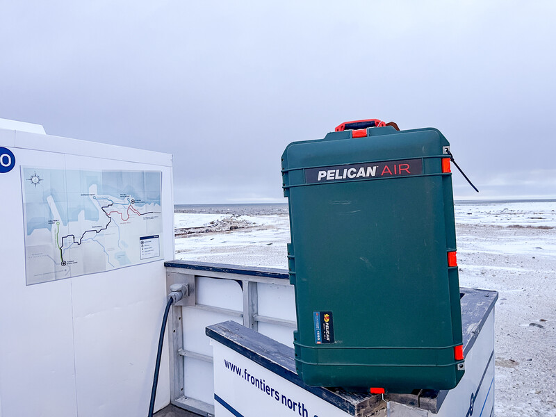 Green Pelican Air cooler with orange handles secured to a white boat railing, with rough ocean waves visible in the background.