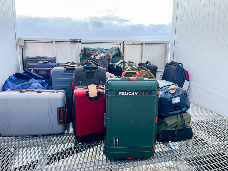 Collection of hard-shell luggage and travel cases arranged inside a cargo container with overhead lighting.