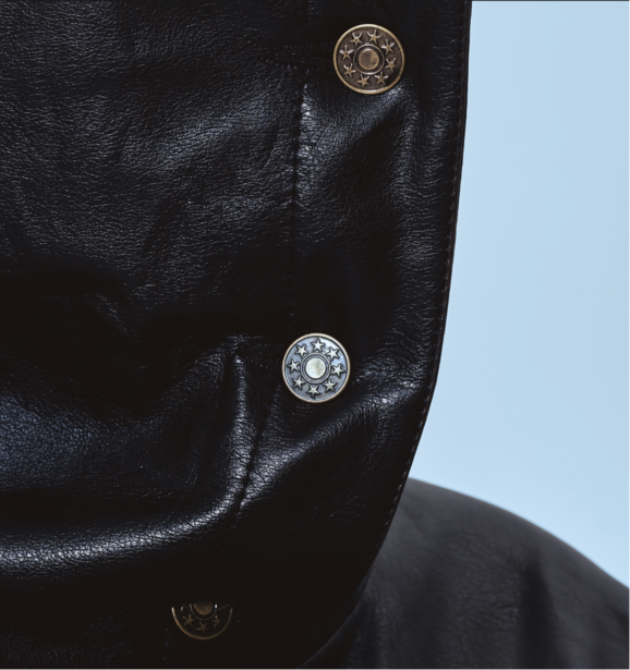 Close-up of black leather jacket with three ornate metal buttons against light blue background.