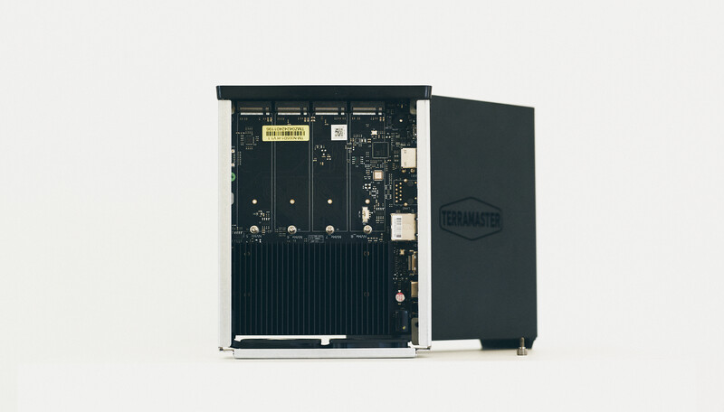 Opened computer server or storage device showing internal circuit board and multiple drive bays against light background.