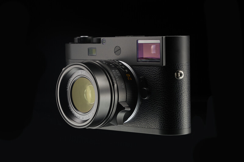Rangefinder camera with silver top plate and black body against dark background.