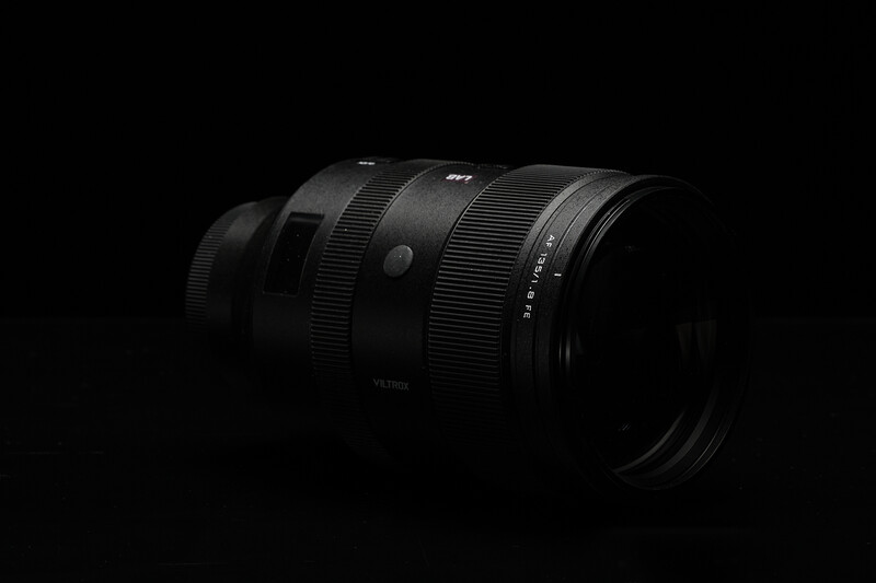 Dark telephoto lens with ribbed focus ring and aperture markings, shot against black background.
