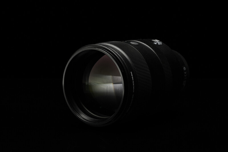 Black telephoto lens photographed against a dark background with dramatic side lighting.