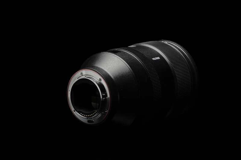 Telephoto lens mounted on camera body, rear element visible, shot against black background.