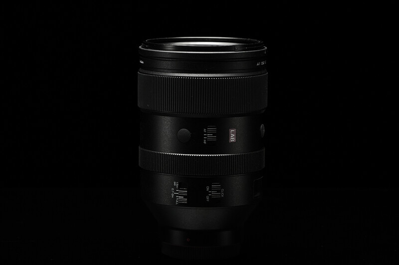 Black telephoto lens with distance markings and control rings against dark background.
