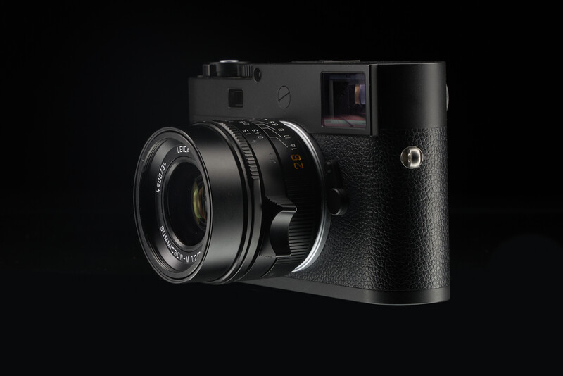 Black rangefinder camera with attached lens against dark background.