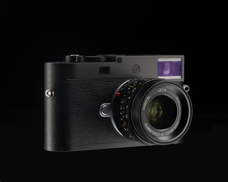 Black rangefinder camera with attached lens and extended LCD screen viewed against black background.