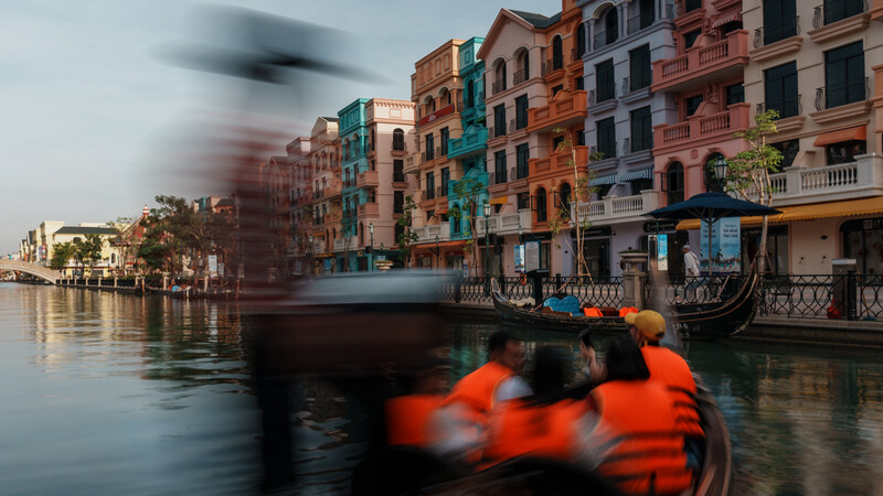 Gondola with blurred passengers in orange life jackets passing colorful waterfront buildings in Venice.