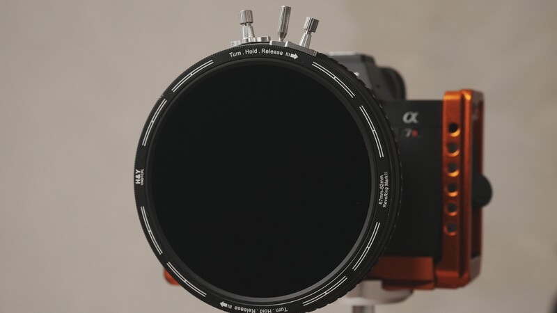 Circular neutral density filter mounted on a matte box with adjustment knobs and an orange-red wooden side arm.