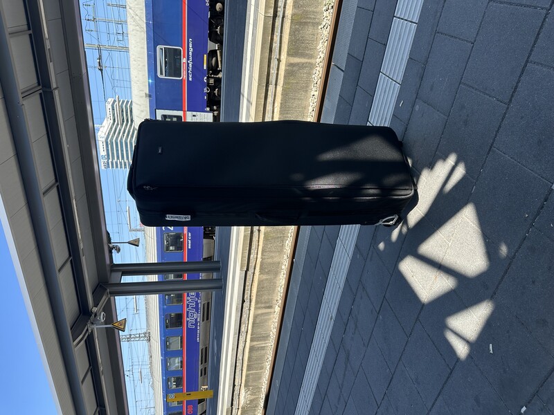 Black rolling suitcase on a train platform casting a sharp shadow in bright sunlight.