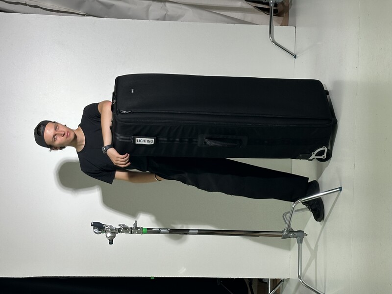 Male subject posing with a large black rolling suitcase in a studio setting with controlled lighting.