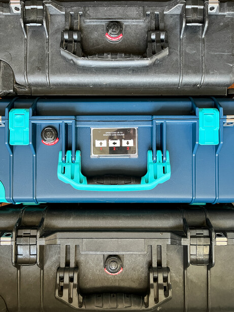 Three plastic equipment cases stacked vertically in black, blue, and gray colors with latches and handles.