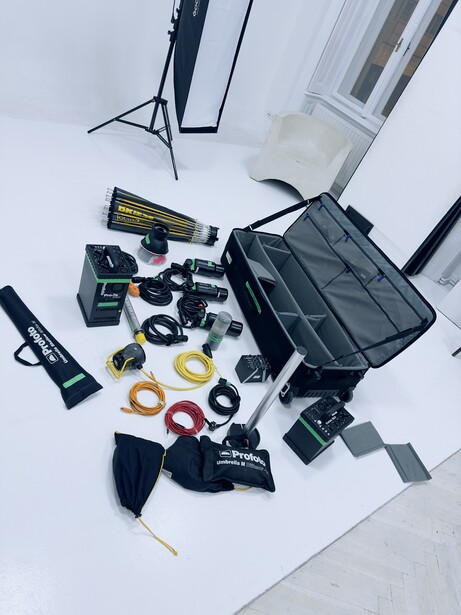 Photography equipment and accessories arranged flat-lay style on white paper, including lighting stands, softbox, cables, and black carrying case.