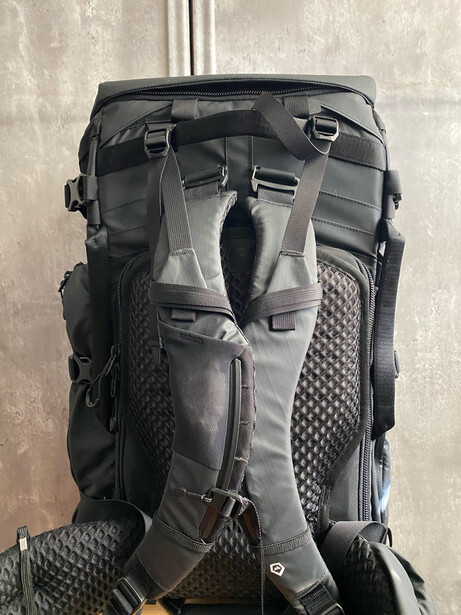 Back view of a dark gray and black hiking backpack with multiple compartments and mesh side pockets.