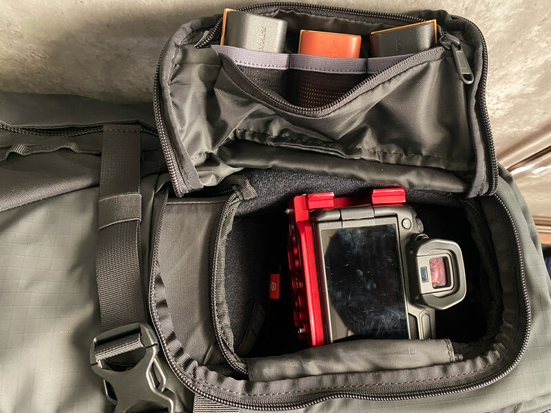 Open camera bag displaying compact digital cameras, batteries, and memory cards organized in compartments.
