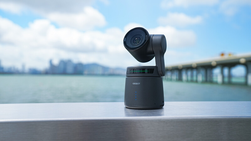 Black motorized PTZ camera mounted on a metal railing overlooking a bay with a bridge and city skyline in the background.