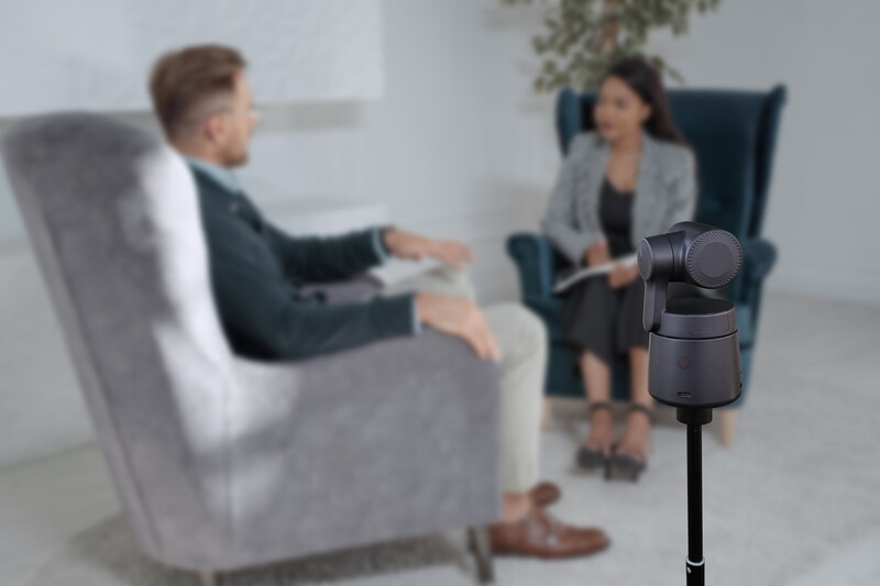Microphone on stand positioned in foreground with two people in conversation blurred in background.