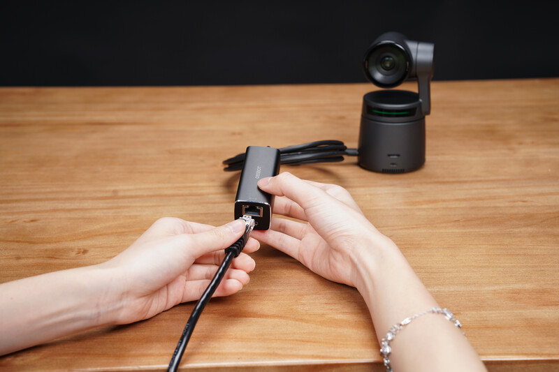 Hands holding a gimbal stabilizer cable with a motorized camera head on a wooden surface.