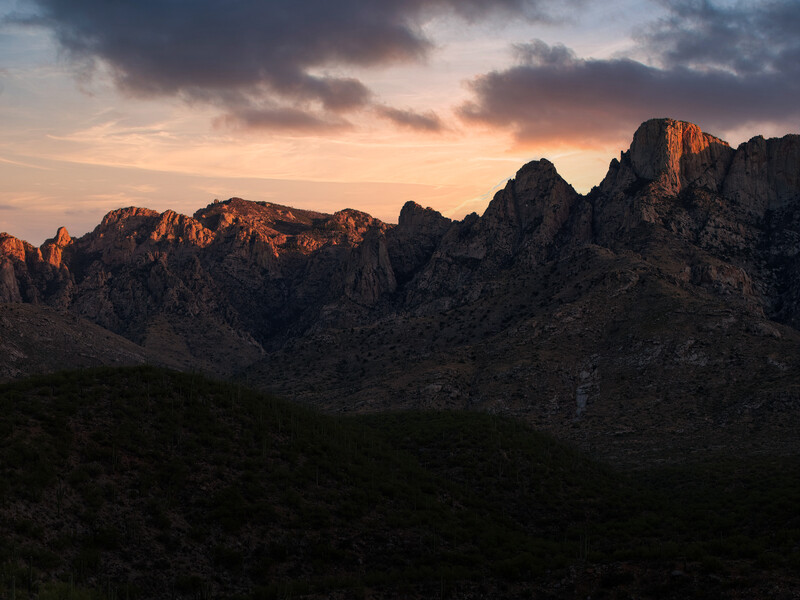 Jagged rocky peaks lit by golden sunset light against a twilight sky with storm clouds.