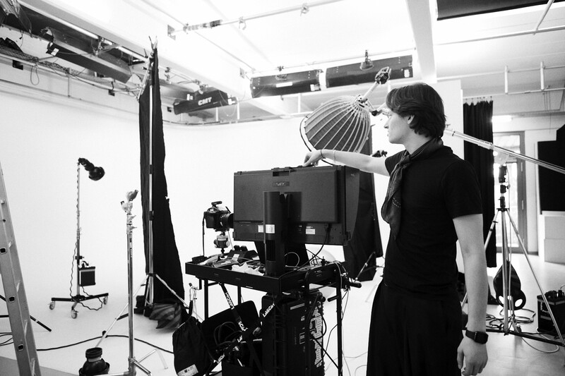 Videographer operating a camera on a tripod in a professional studio with studio lighting setup.