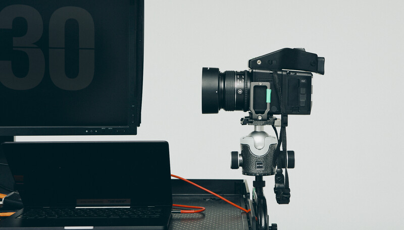 Professional cinema camera mounted on a tripod head with a telephoto lens attached, positioned next to a laptop and numbered slate.
