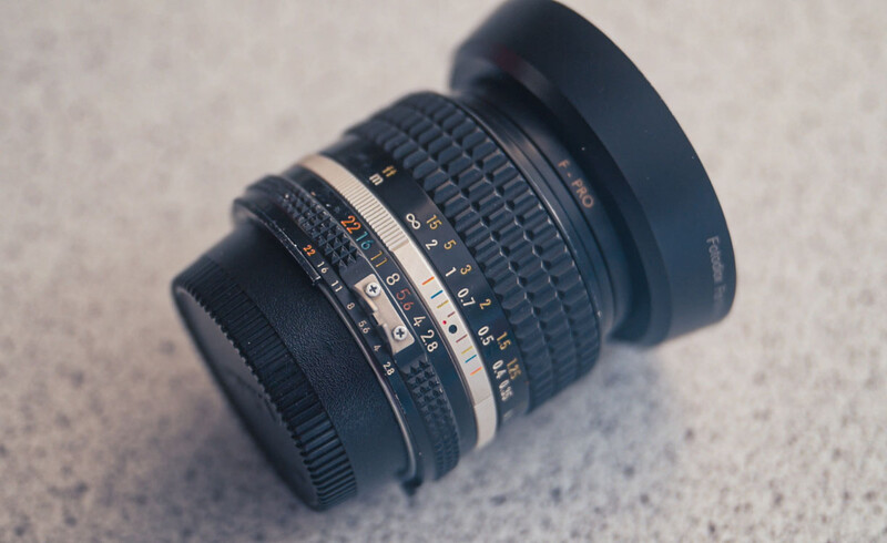 Vintage manual focus camera lens with white focusing ring and distance scale markings on concrete surface.