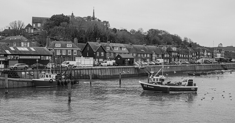 Fishing boats moored at a harbor with Georgian townhouses lining the waterfront.