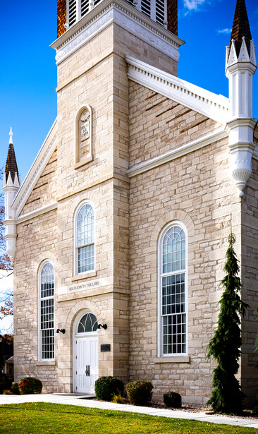 Stone church facade with steeple tower and arched windows against clear blue sky.