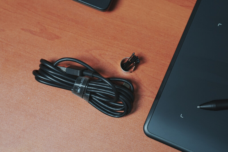 Black coiled power cable and connector adapter on a wooden desk surface next to camera equipment.