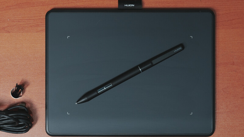 Huion graphics tablet with stylus pen on wooden surface next to USB cable and power adapter.