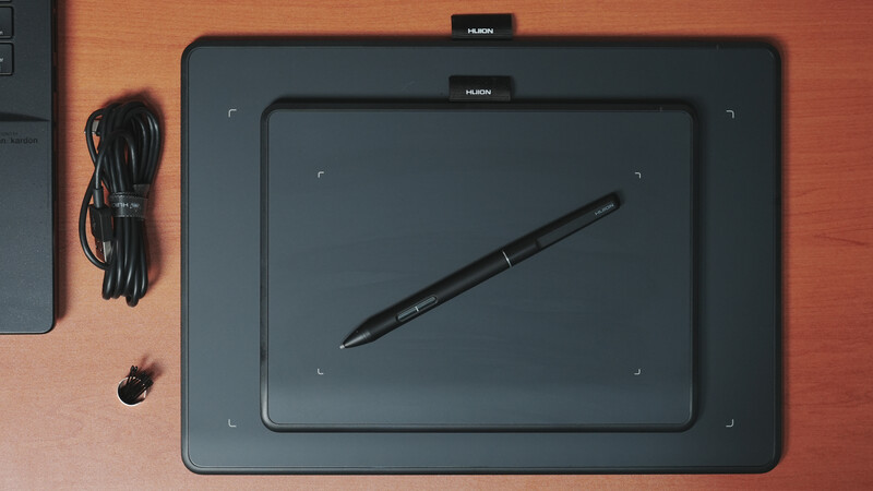Huion graphics tablet with stylus on wooden surface next to coiled cable.
