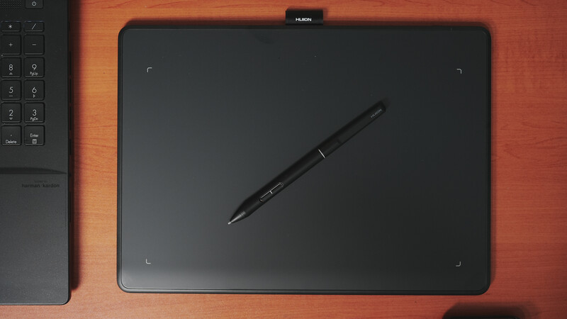 Huion graphics tablet with stylus pen on wooden desk surface next to keyboard.