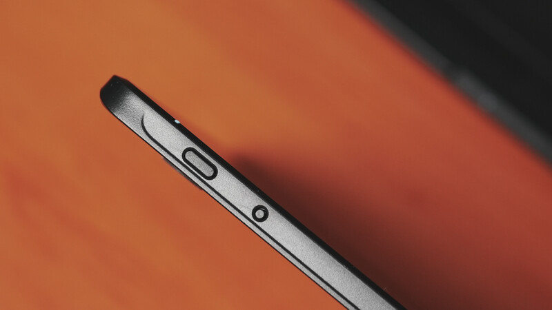 Close-up of a smartphone edge showing volume and power buttons against an orange background.