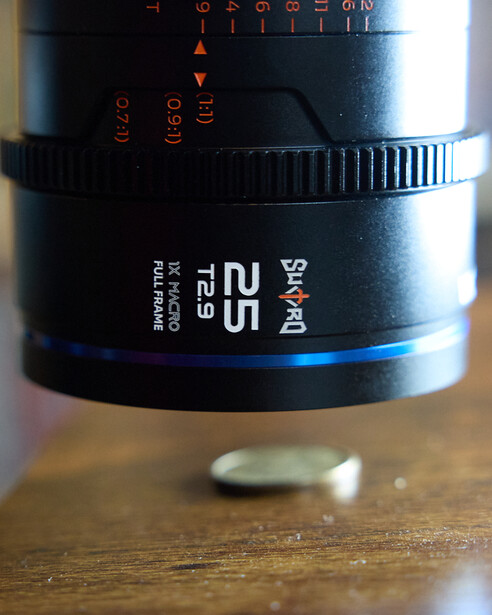 Zeiss 25mm f/2.8 macro lens mounted on wooden surface with focus ring and aperture markings visible.
