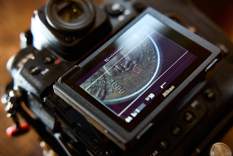 Professional video camera with articulating LCD screen displaying a waveform monitor with purple and gray tones.