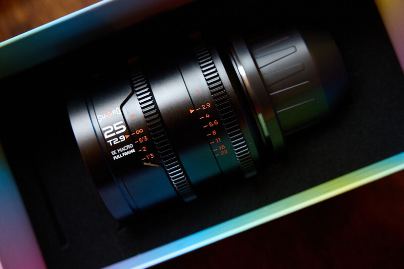 Cinema lens with focus and iris markings mounted on a blue-green surface.