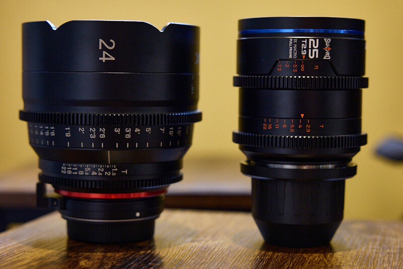 Two cinema lenses with focus rings and depth-of-field markings displayed side by side on a wooden surface.