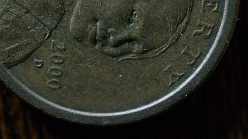 Close-up of a worn metal coin showing a profile portrait and partial text markings.