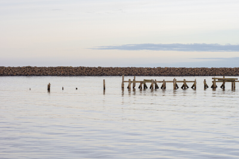 Weathered wooden pilings and dock structures partially submerged in calm water at dusk.