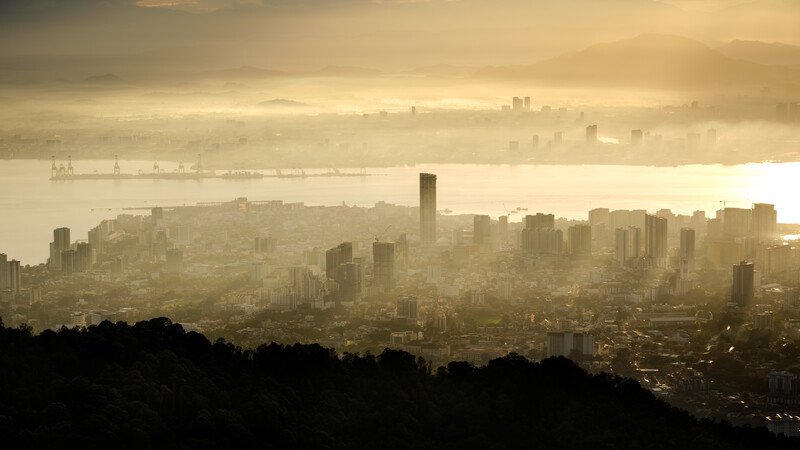 Dense urban cityscape shrouded in golden haze and fog, with bay waters visible in the background.