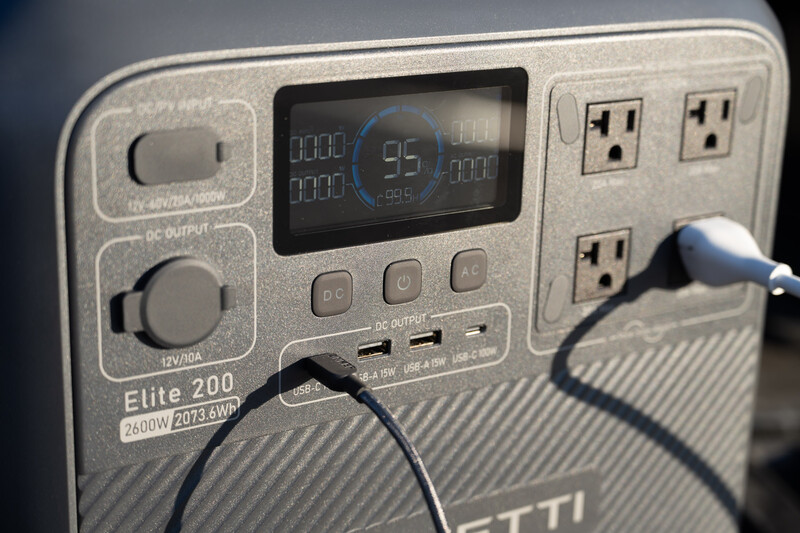 Portable power station with digital display showing battery percentage and multiple AC outlets with charging cables connected.