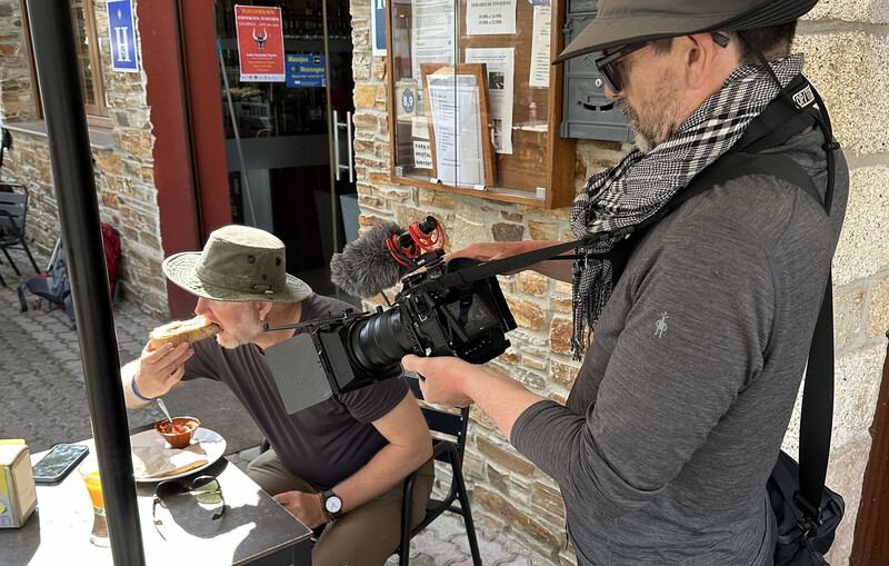 Cameraman filming a person eating at an outdoor street location.