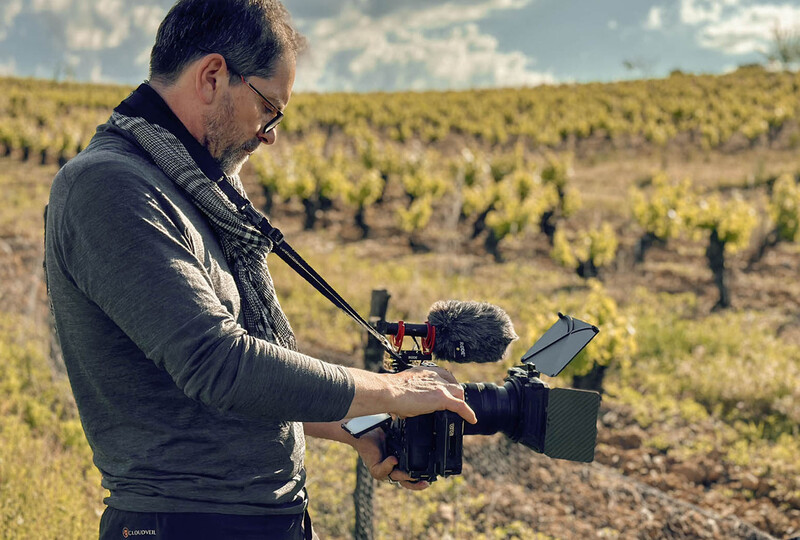 Filmmaker holding a professional camera rig with shotgun microphone in a vineyard.