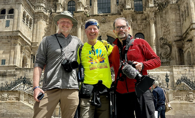 Three men posing in front of a large stone cathedral building, smiling at the camera.