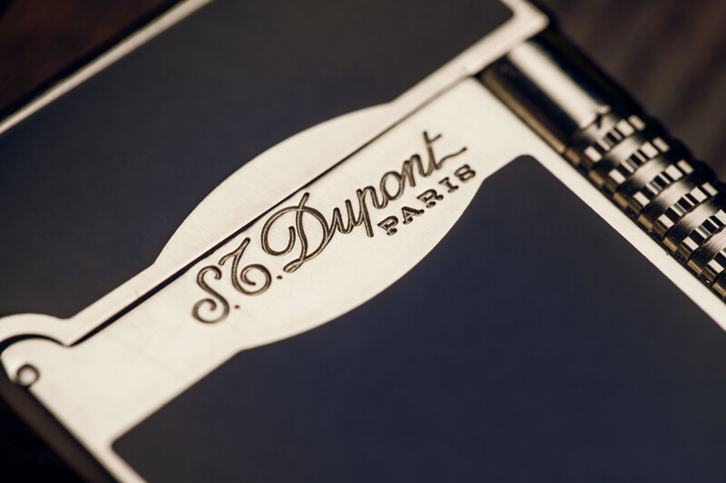 S.T. Dupont lighter with engraved logo on white metal casing against dark background.