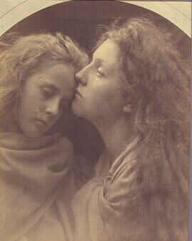 Two figures with long, flowing hair in profile, posed closely together in a soft-focus portrait.