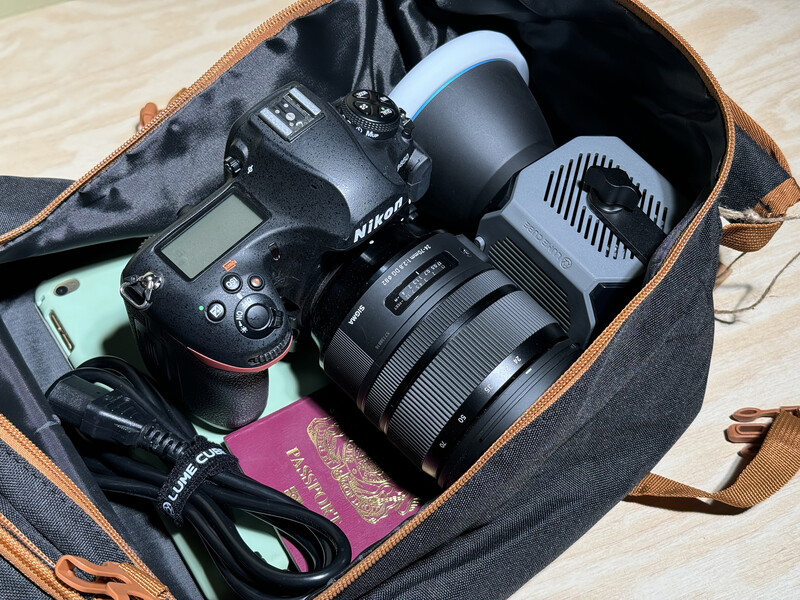 Nikon DSLR camera with telephoto lens and accessories packed in a canvas and leather camera bag.