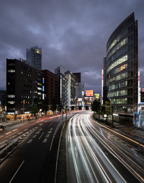 Urban street at dusk with light trails from moving traffic between illuminated office buildings.