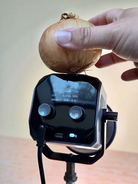 Hand holding a round object above a black lighting instrument with two circular apertures.