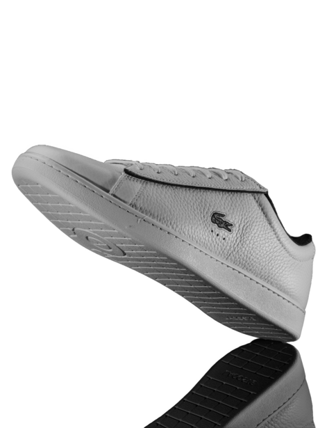White leather low-top sneaker photographed against black background with dramatic side lighting.